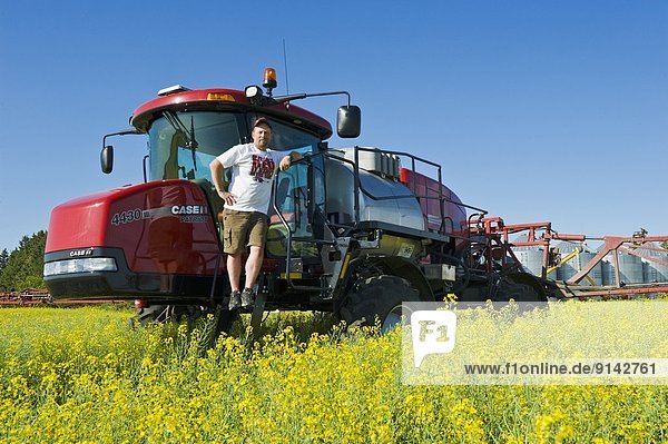 Farmer on high clearance sprayer in canola field near Dugald  Manitoba  Canada