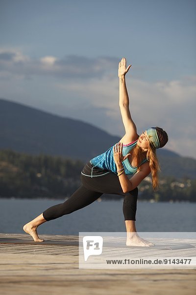 Young woman practicing yoga on dock overlooking Kalamalka Lake  near Vernon  Okanagan  British Columbia  Canada