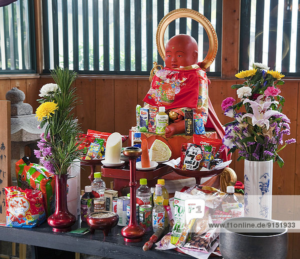 Jizo is a Bodhisattva decked in a red cap and bib and it is surrounded by offerings Koyasan  Japan