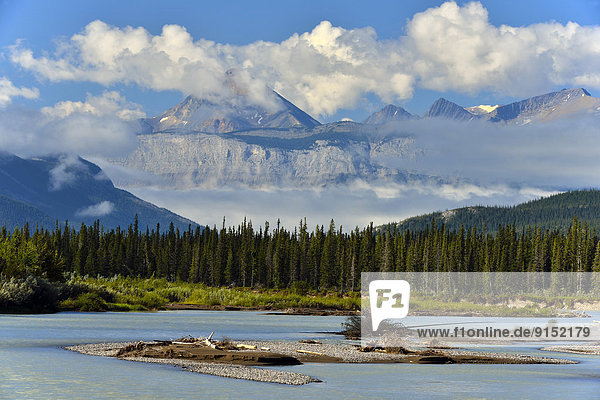 An image of Pyramid mountain towering over the other mountain ridges with cloud and mist captured on a summer morning along the Athabasca river in Jasper National Park Alberta  Canada.