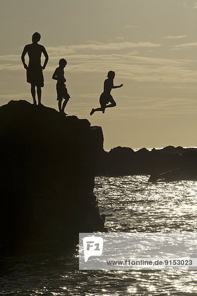 Youth jumping from the rock into the sea at sunset