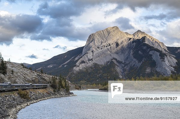 Passenger train along the Athabasca river and Roche Miette at sunset in the Rocky Mountains  Alberta  Canada.