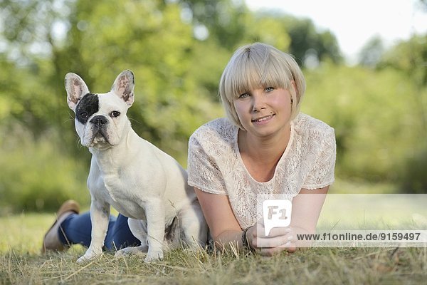 Frau liegt auf einer Wiese mit einer sieben Monate alten Französischen Bulldogge