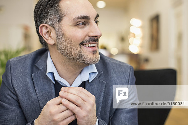 Smiling mid adult businessman with hands clasped looking away in office