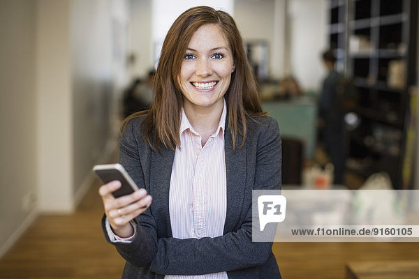 Porträt einer lächelnden Geschäftsfrau mit Handy im Büro