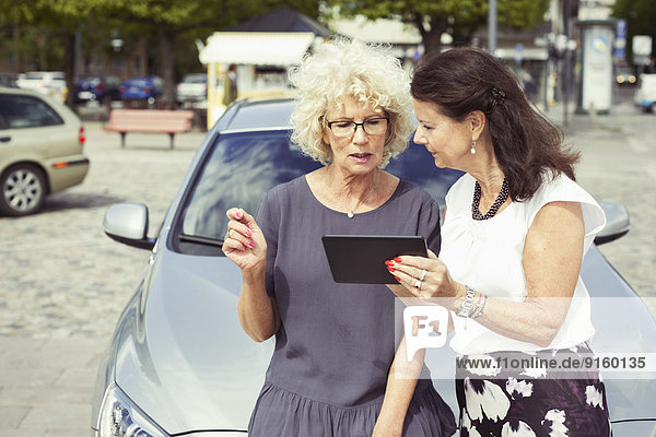 Senioren-Freundinnen benutzen digitales Tablett gegen Auto auf der Straße