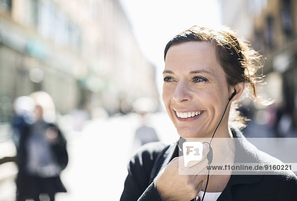 Smiling mature businesswoman talking through headphones on city street