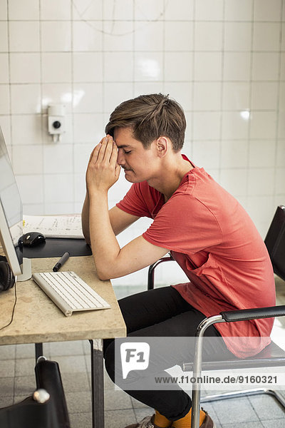 Worried young businessman with hands clasped sitting at computer desk in new office