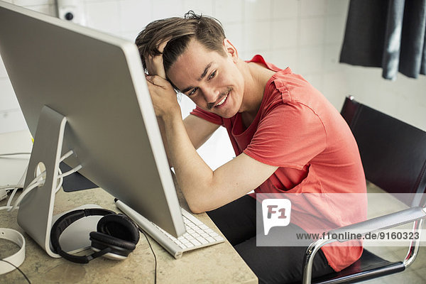 Nachdenklicher junger Geschäftsmann am Computertisch im neuen Büro