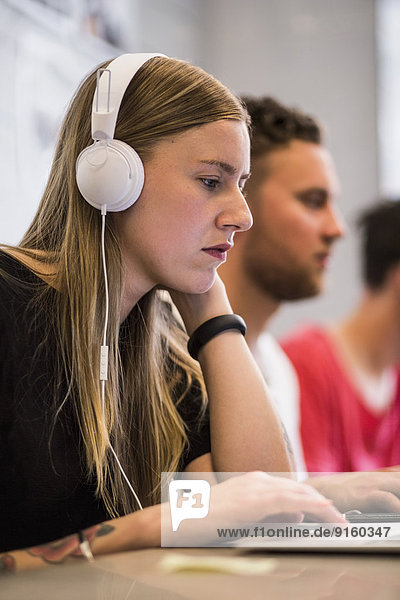 Junge Geschäftsfrau hört Kopfhörer  während sie den Laptop im neuen Büro benutzt.
