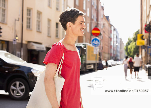 Seitenansicht des glücklichen jungen Mannes mit Tasche auf der Stadtstraße
