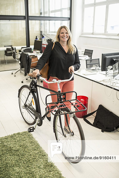 Portrait of businesswoman with bicycle walking in creative office