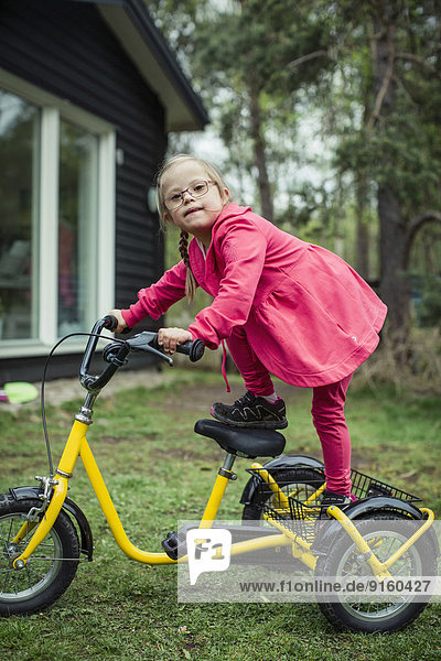 Portrait eines Mädchens mit Down-Syndrom  das auf dem Fahrrad im Rasen balanciert.