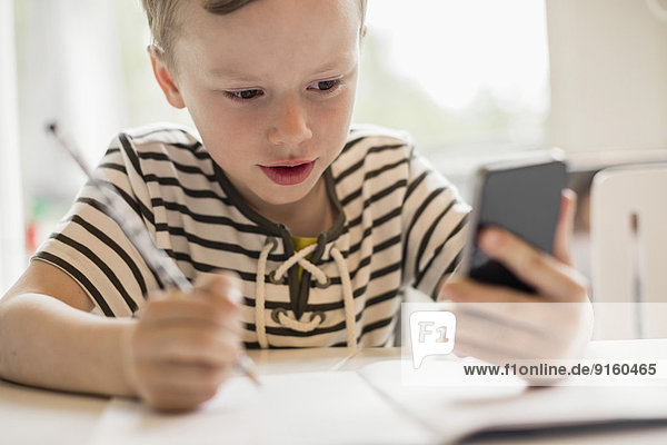 Junge mit Smartphone beim Schreiben am Tisch