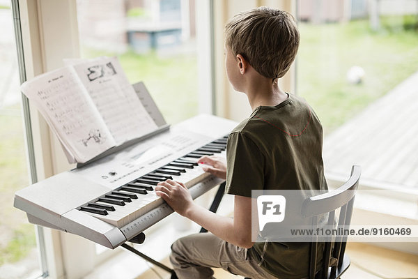 Rückansicht des Jungen  der zu Hause Klavier spielt