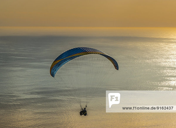 Paraglider-Tandemsprung  Gleitschirm fliegt über dem Meer bei Sonnenuntergang  Kapstadt  Westkap  Republik Südafrika