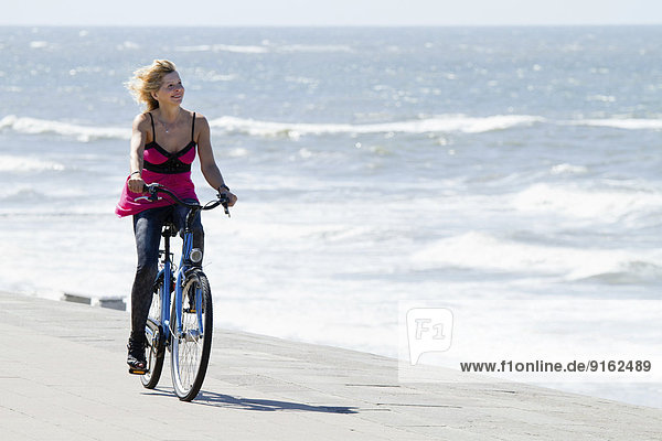 Frau im Sommerkleid fährt Fahrrad am Meer  Norderney  Niedersachsen  Deutschland