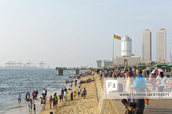 Menschen spazieren an der Strandpromenade  Galle Face  Hochhäuser und Hafen dahinter  Colombo  Sri Lanka