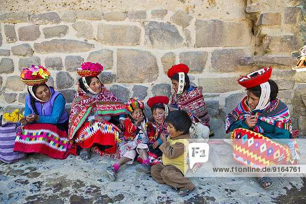 Women and children in traditional dress of the Quechua Indians sitting on the floor in front of a wall Ollantaytambo Urubamba Valley Peru