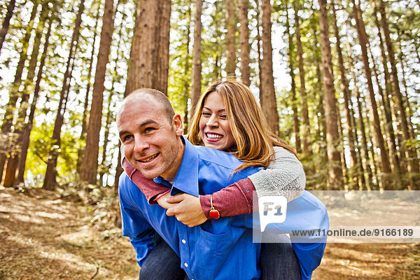 Hispanic man carrying girlfriend piggy back in forest