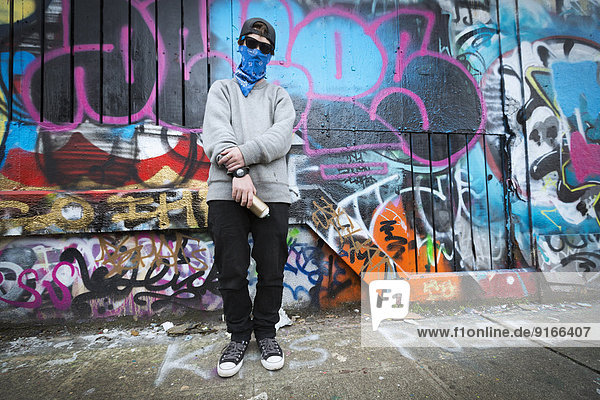 Caucasian teenage boy standing by graffiti wall