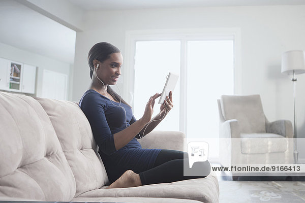 Black woman using digital tablet on sofa