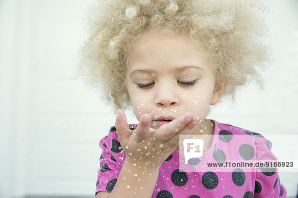 Mixed race girl blowing sparkles from hand