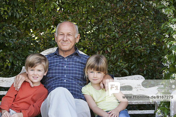 Grandfather sitting with grandchildren on garden bench