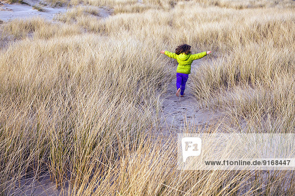Caucasian girl running in grassy sand dune Caucasian girl running in grassy sand dune