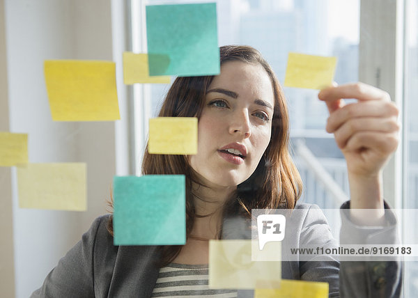 Businesswoman reading sticky notes on glass