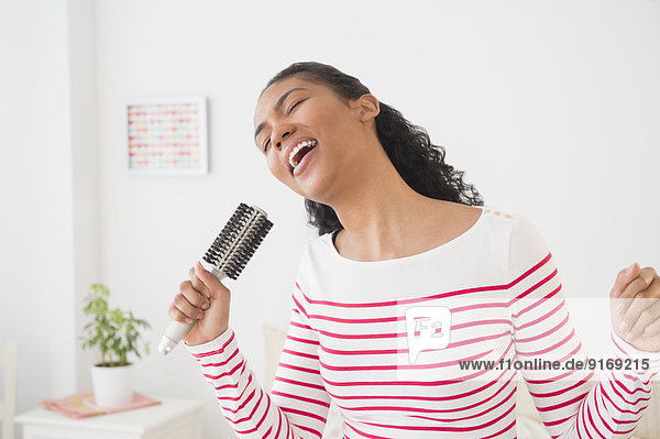 Mixed race woman singing into hairbrush