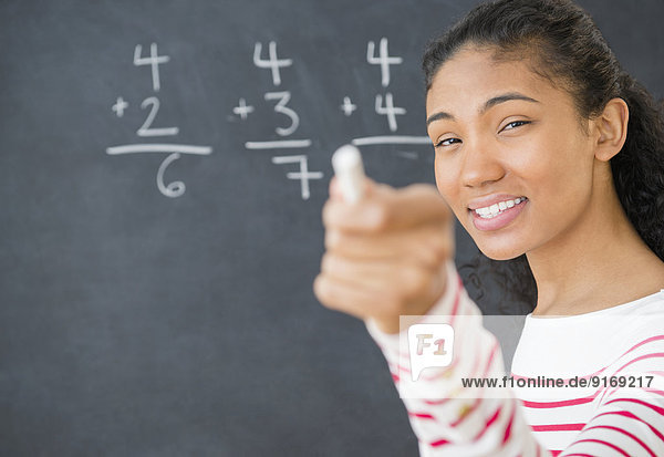 Mixed race teacher doing math on chalkboard