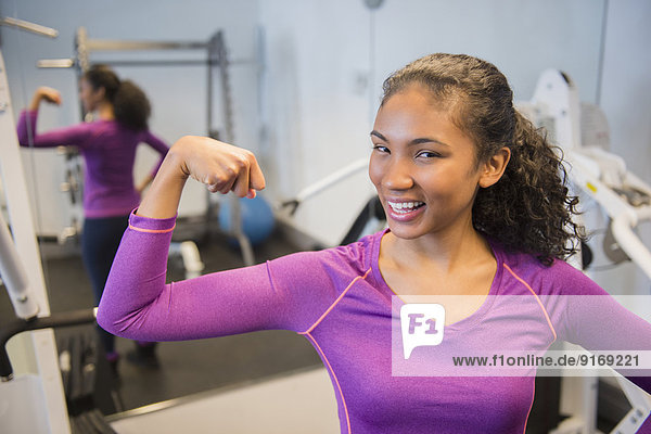 Mixed race woman flexing muscles in gym