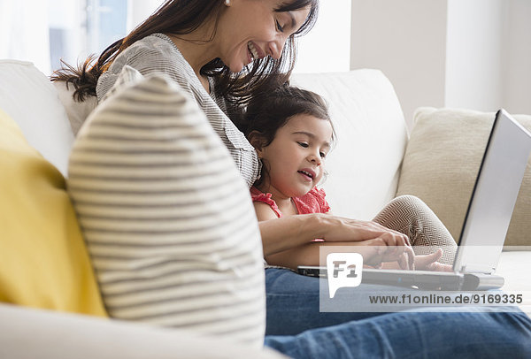 Hispanic mother and daughter using laptop on sofa