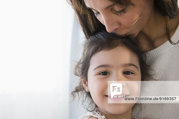 Hispanic mother kissing top of daughter's head