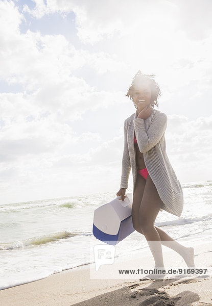 African American woman carrying cooler on beach