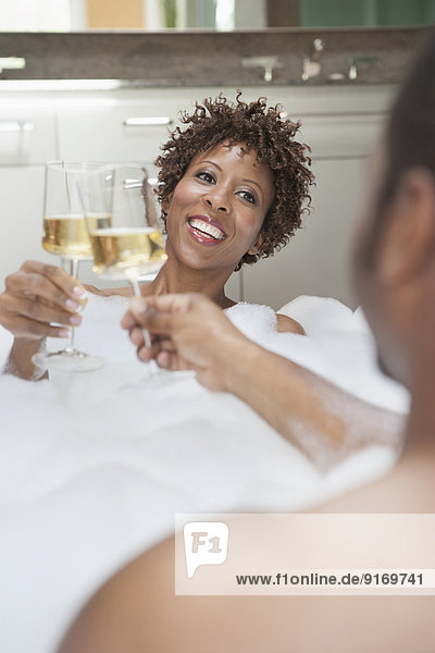 African American couple drinking champagne in bath