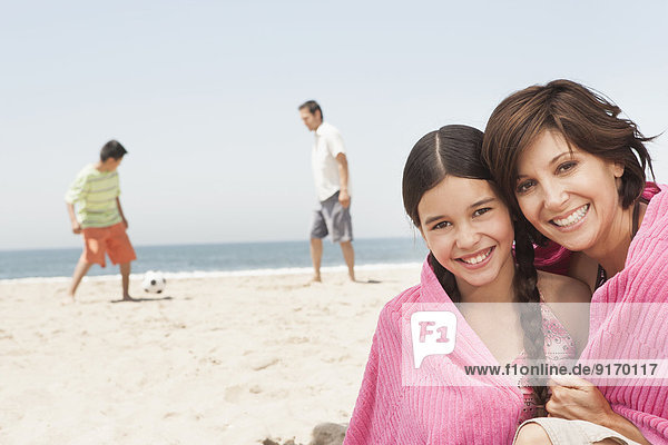 Mother and daughter wrapped in towel on beach