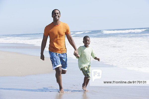 Father and son walking in waves on beach