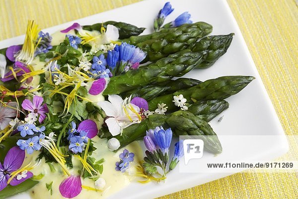 Green asparagus with a saffron sauce and edible flowers on plate