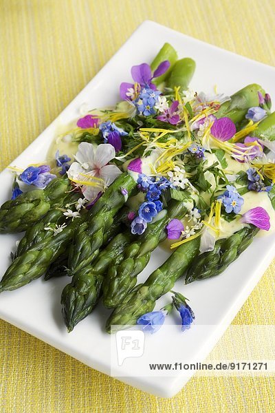 Green asparagus with a saffron sauce and edible flowers on plate