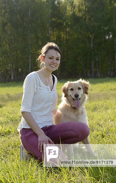 Young woman sitting with Golden Retriever on meadow