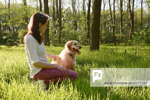 Junge Frau sitzend mit Golden Retriever auf der Wiese