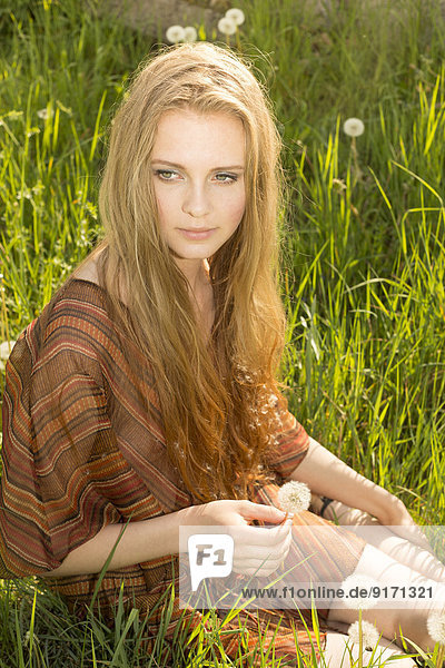 Porträt einer jungen Frau,  die auf einer Sommerwiese sitzt.