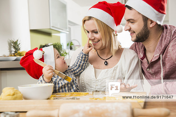 Familie mit Weihnachtsmützen beim Backen in der Küche