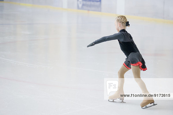 Young female figure skater moving on ice rink at competition