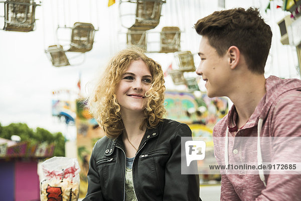 Portrait of teenage couple at fun fair with chairoplane in the background