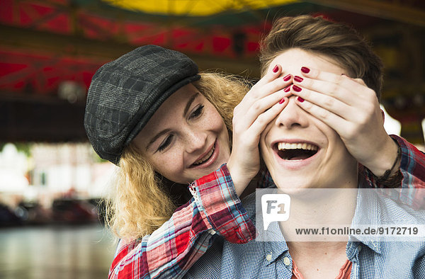 Teenager-Mädchen  das die Augen ihres Freundes mit den Händen bedeckt.