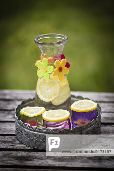 Tablett  Karaffe mit Limonade und Zitronenscheiben auf bunten Gläsern