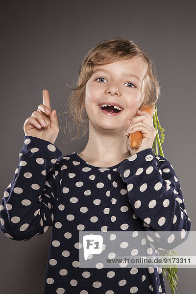Portrait of little girl using carrot as a phone